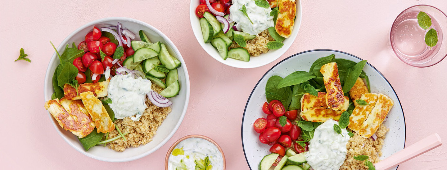 Halloumi-bowl. K-Ruoan reseptin kuva, jossa lautasia vaaleapunaisella taustalla. Salaatissa muun muassa halloumia, kurkkua ja kirsikkitomaatteja.