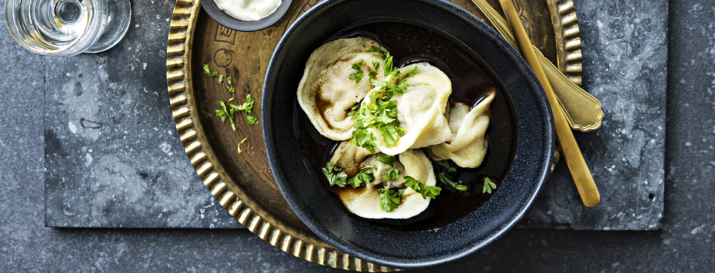 Pelmenit lihatäytteellä pyöreässä tummassa kulhossa keittoliemessä. Pelmenien päälle on ripoteltu tuoretta persiljaa. K-Ruoka resepti.