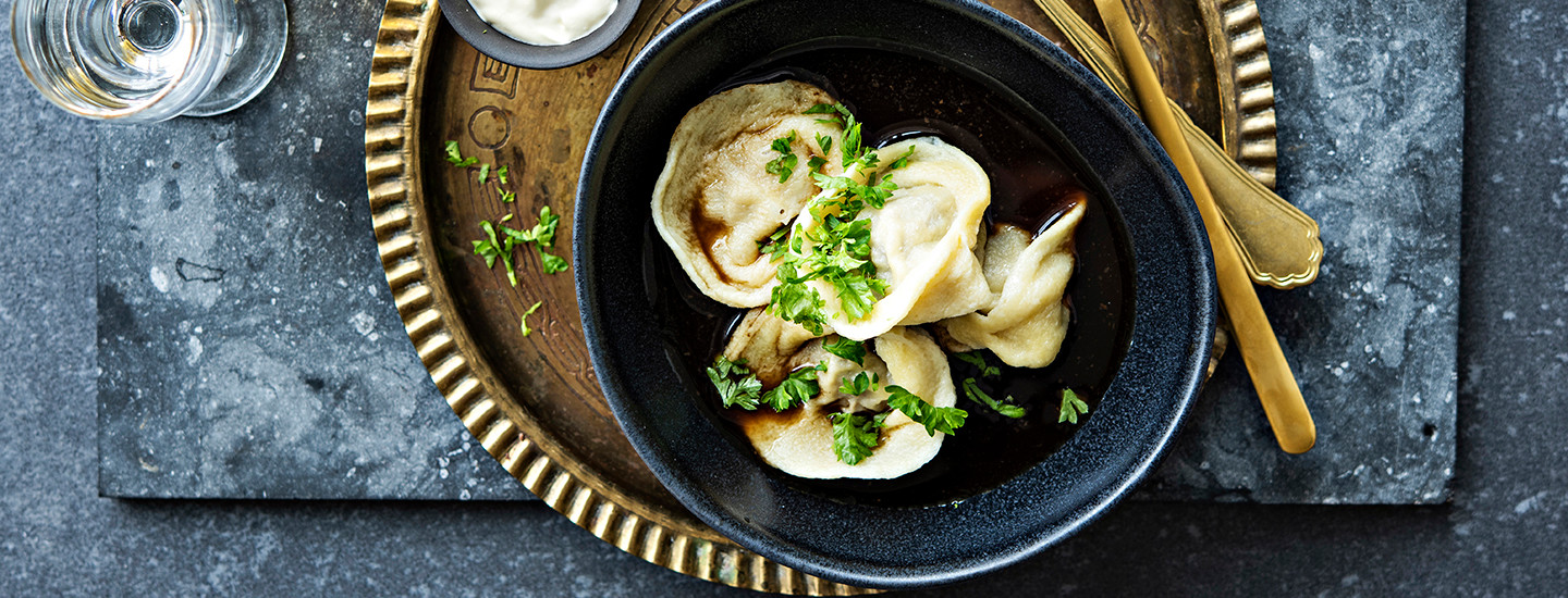 Pelmenit lihatäytteellä pyöreässä tummassa kulhossa keittoliemessä. Pelmenien päälle on ripoteltu tuoretta persiljaa. K-Ruoka resepti.