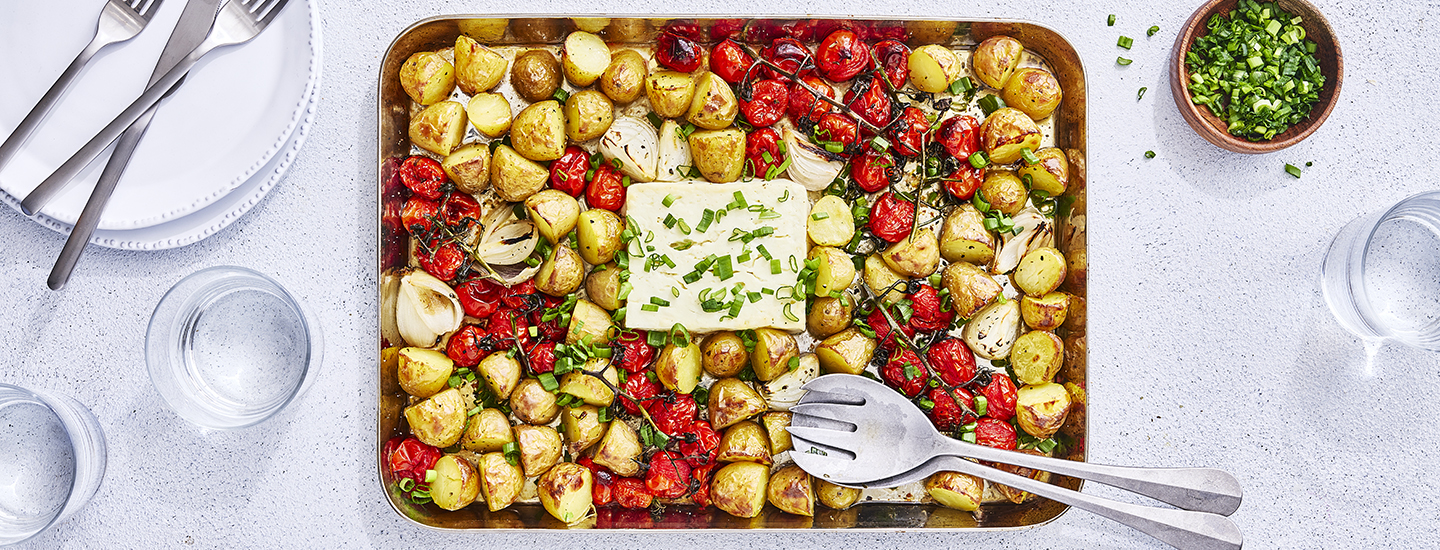 Varhaisperunoita lohkoina ja tomaattiterttuja uunivuoassa, vuoan keskellä on fetajuustolohko. Kasvikset ja feta on paahdettu grillissä ja ne on koristeltu ruohosipulilla. K-Ruoka grillausresepti.