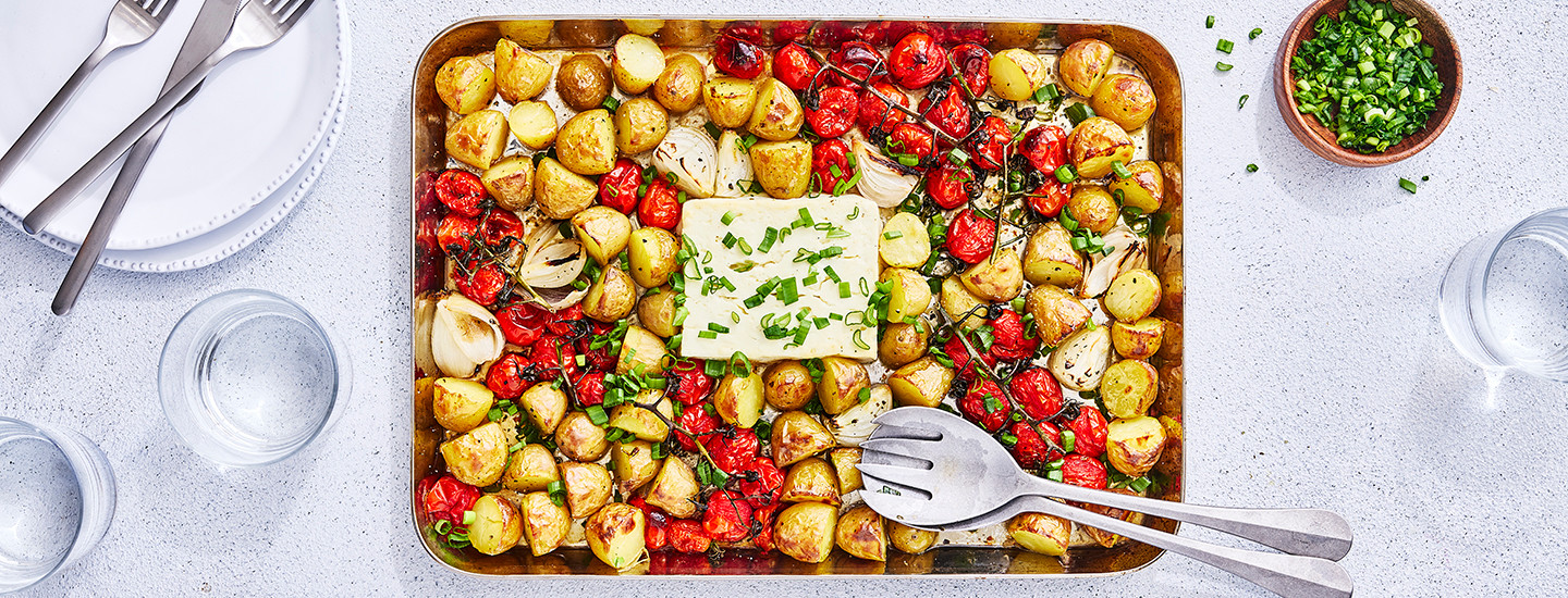 Varhaisperunoita lohkoina ja tomaattiterttuja uunivuoassa, vuoan keskellä on fetajuustolohko. Kasvikset ja feta on paahdettu grillissä ja ne on koristeltu ruohosipulilla. K-Ruoka grillausresepti.