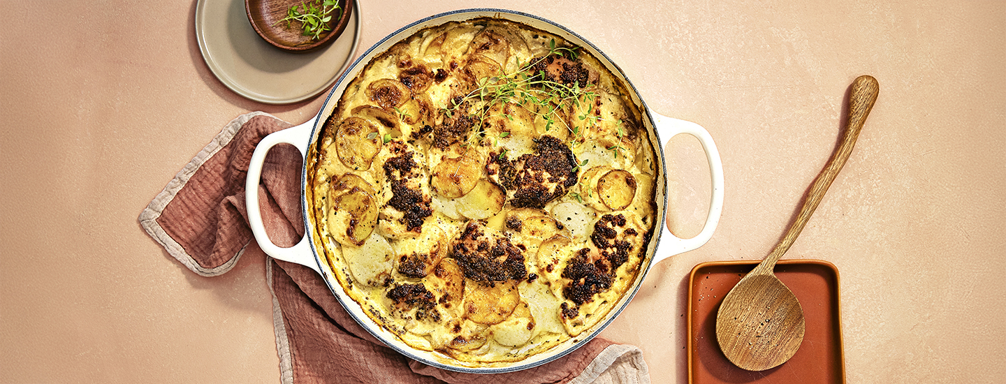 Kana-perunaruokaa pyöreässä uunivuoassa. Kana-perunavuoan päälle on ripoteltu tuoreita yrttejä. K-Ruoka arkiruokaresepti.