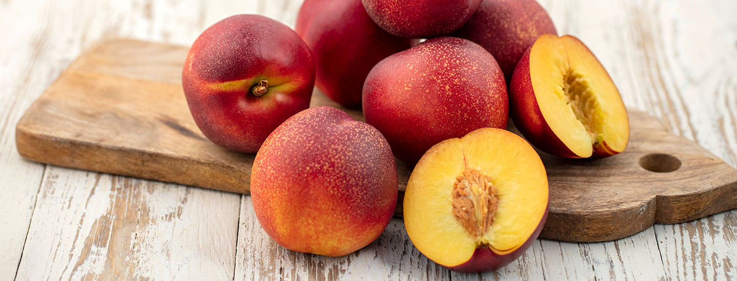 Tuoreita nektariineja kokonaisena ja halkaistuna puisen leikkuulaudan päällä.