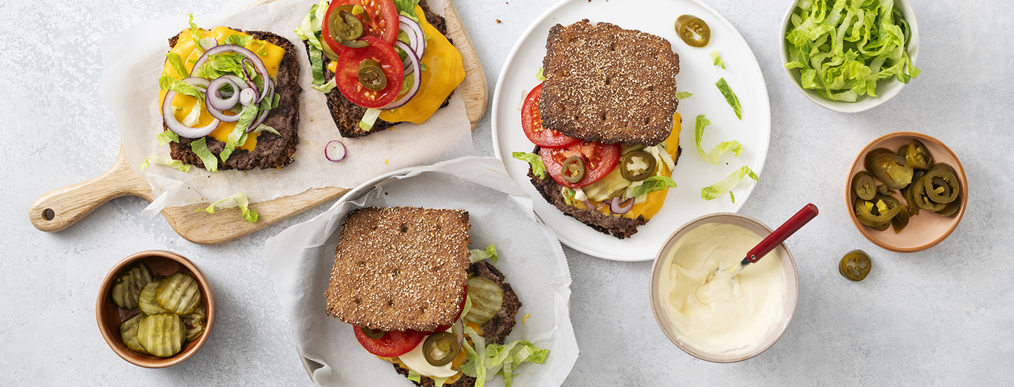 Ruis smash burgereita lautasilla. Ruisleipien välissä on paistettua jauhelihaa, cheddarjuustoa, kasviksia ja kastiketta. K-Ruoka grillausresepti.