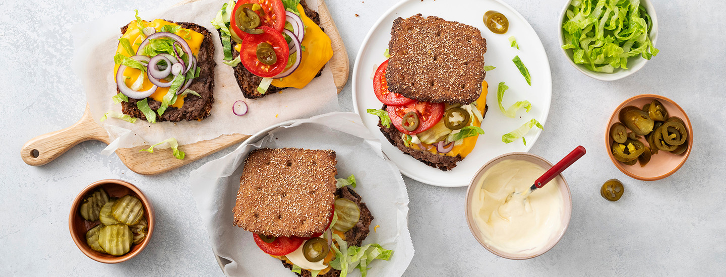 Ruis smash burgereita lautasilla. Ruisleipien välissä on paistettua jauhelihaa, cheddarjuustoa, kasviksia ja kastiketta. K-Ruoka grillausresepti.