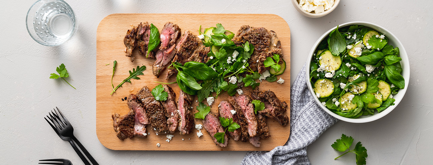 Karitsan grillipihvejä puisella leikkuulaudalla. Pihvien seassa on vihersalaattia ja fetajuustoa. K-Ruoka resepti.