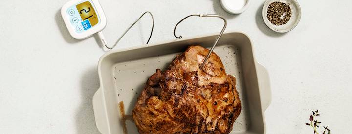 Karitsan valmistuksen kolmas vaihe: lämpömittarin käyttö ja paistin paisto. Karitsanpaisti on asetettu valkoiseen uunivuokaan. Paistiin on kiinnitetty lämpömittari.