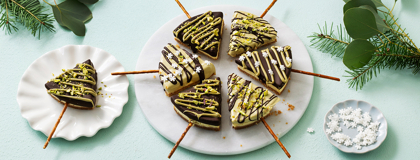 Juustokakkupaloja tarjoilulautasella leikattuna kolmion muotoisiksi. Juustokakut on päällystetty tummalla suklaalla ja valkosuklaalla sekä erilaisilla jouluisilla syötävillä koristeilla. K-Ruoka jouluresepti.