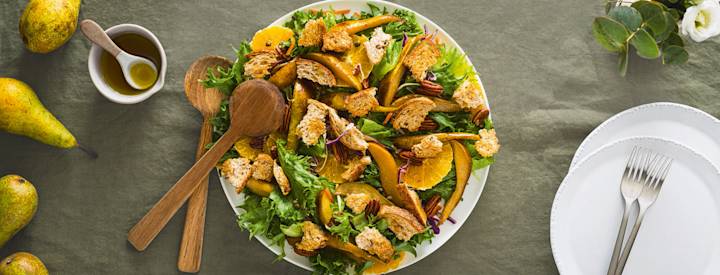 Talvipanzanellasalaattia valkoisella tarjoilulautasella. Salaatissa on vihersalaattia, appelsiinia, paistettuja päärynöitä, pekaanipähkinöitä ja paahdettua leipää. K-Ruoka salaattiresepti.