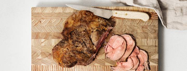 Karitsan valmistuksen neljäs vaihe: karitsanpaistin vetäytyminen ja viipalointi. Kypsä karitsanpaisti on puisella leikkuulaudalla. Paistista on leikattu viipaleita veitsellä.