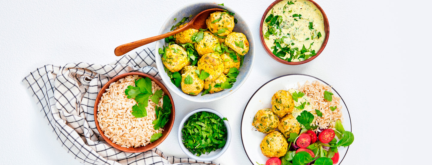 Kanapyöryköitä pienessä kulhossa, pyöryköiden päälle on ripoteltu tuoreita yrttejä. Kulhon vieressä on toinen, ruskea kulho, jossa on riisiä. Kulhojen vieressä olevalle lautaselle on tehty annos kanapyöryköistä, riisistä ja salaatista. K-Ruoka arkiruokaresepti.