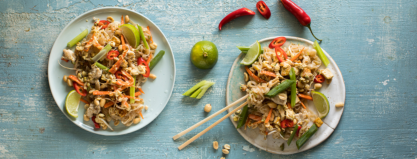 Pad thai -nuudelit kahdella pyöreällä lautasella. Nuudelien seassa on kanaa, kasviksia, limeviipaleita ja tuoretta chiliä. K-Ruoka resepti.