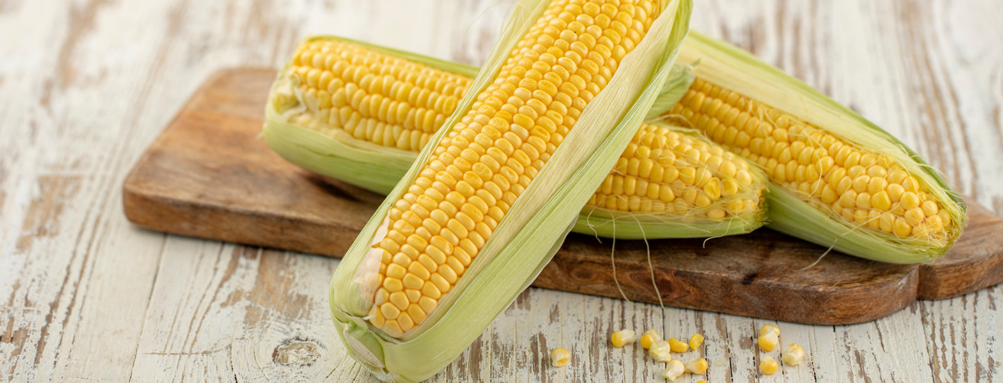 Tuoreita maissintähkiä puisen leikkuulaudan päällä.