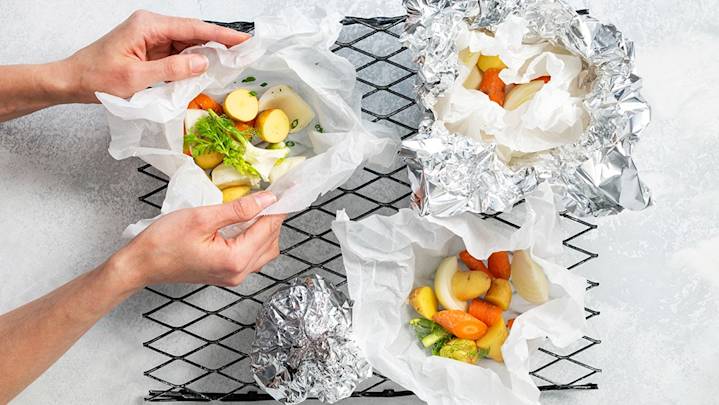 Perunalohkoja, porkkanapaloja ja sipulia yrttien kanssa folio- ja leivinpaperinyyteissä.