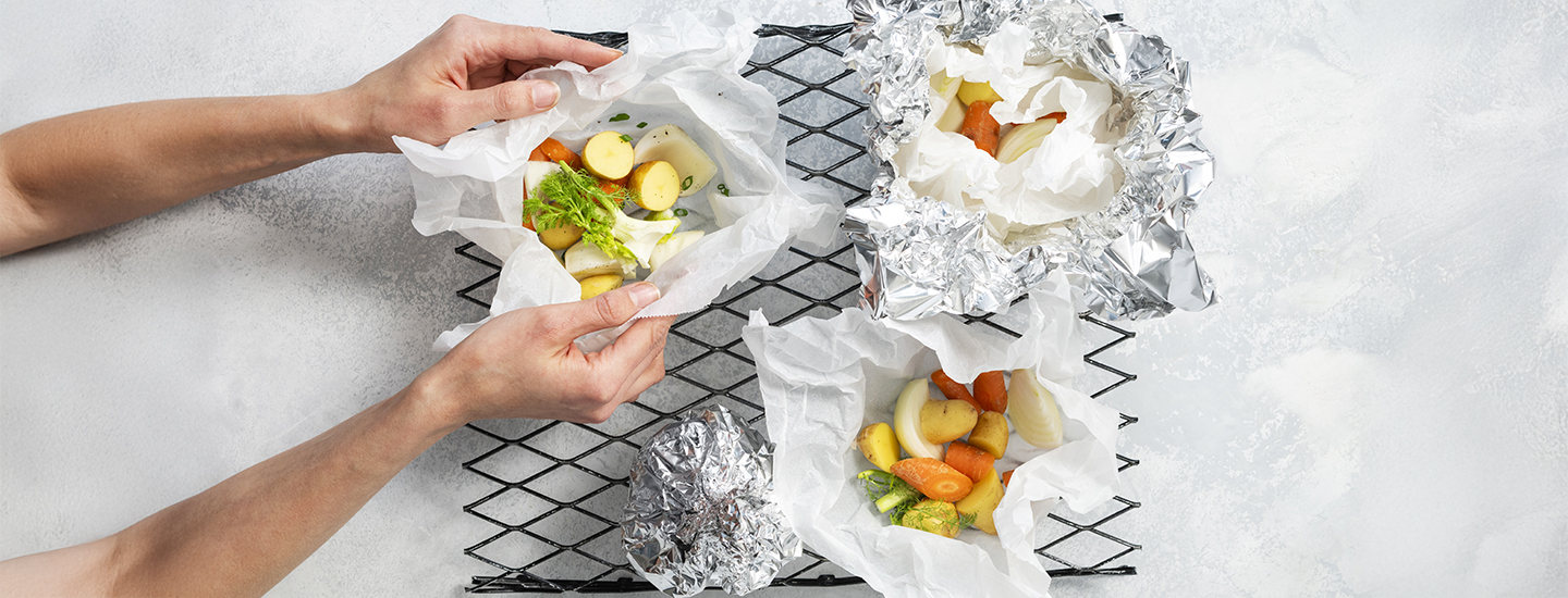 Perunalohkoja, porkkanapaloja ja sipulia yrttien kanssa folio- ja leivinpaperinyyteissä.