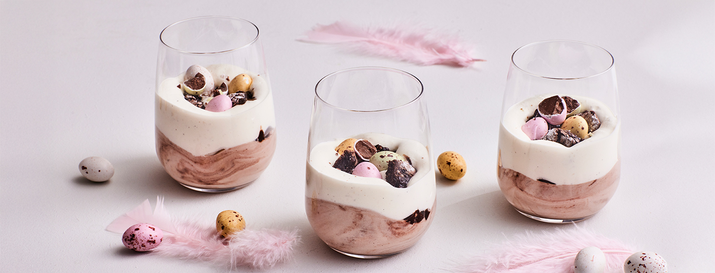 Kermavaahdosta, kaakaojauheesta, mutakakusta ja pääsiäissuklaamunista koottuja jälkiruoka-annoksia laseissa. K-Ruoka pääsiäisresepti.