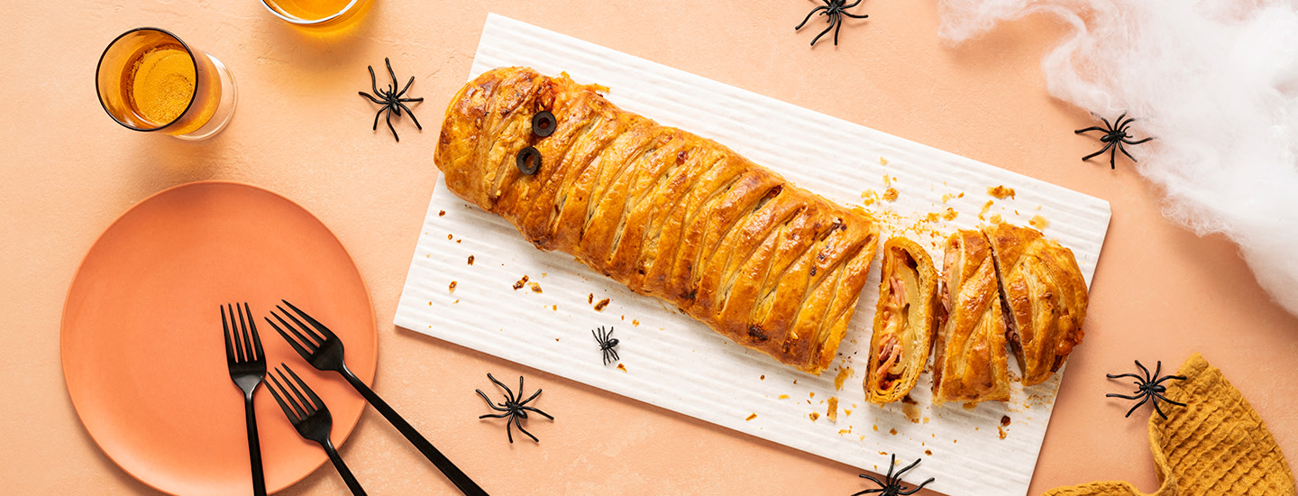 Voitaikinasta tehty letitetty suolainen piirakka valkoisen tarjoilulautasen päällä. Piirakan sisällä on kinkkua, juustoa ja pizzakastiketta. K-Ruoka halloweenresepti.