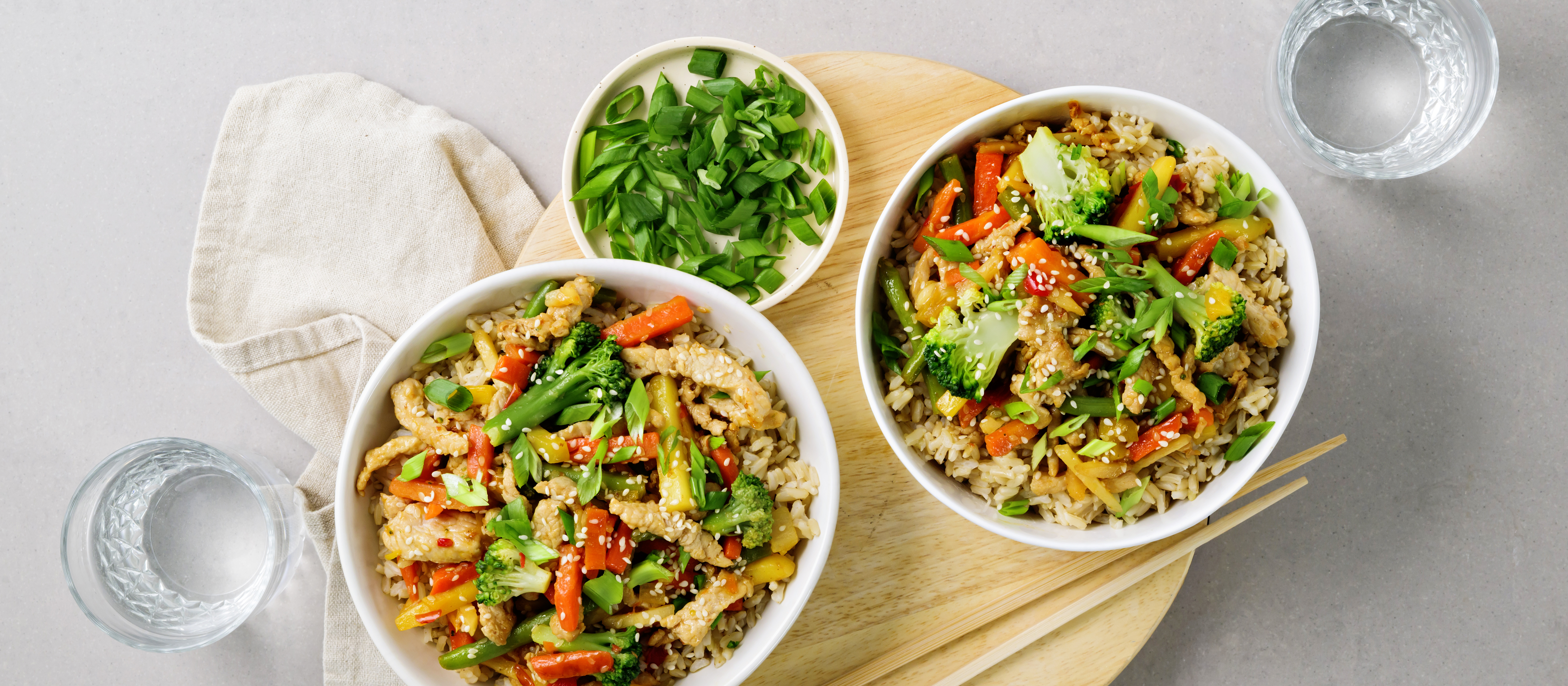 Possuwokkia kahdessa kulhossa. Wokissa on possusuikaleita, kasviksia ja riisiä. K-Ruoka arkiruokaresepti.