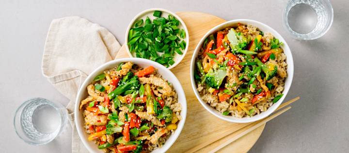 Possuwokkia kahdessa kulhossa. Wokissa on possusuikaleita, kasviksia ja riisiä. K-Ruoka arkiruokaresepti.