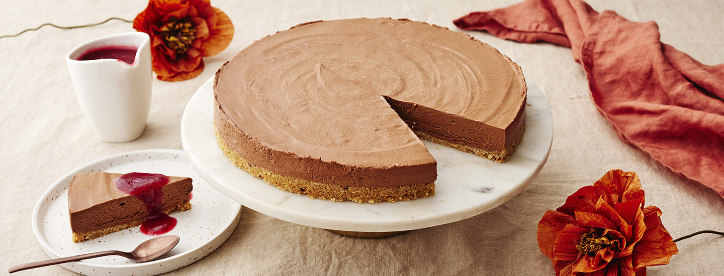 Jäädytetty suklaajuustokakku pyöreällä kakkutarjottimella. Kakusta on leikattu palanen, jonka päälle on lisätty marjakastiketta. K-Ruoka juustokakkuresepti.