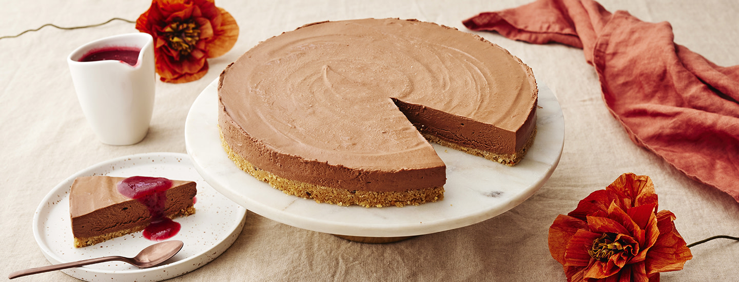 Jäädytetty suklaajuustokakku pyöreällä kakkutarjottimella. Kakusta on leikattu palanen, jonka päälle on lisätty marjakastiketta. K-Ruoka juustokakkuresepti.