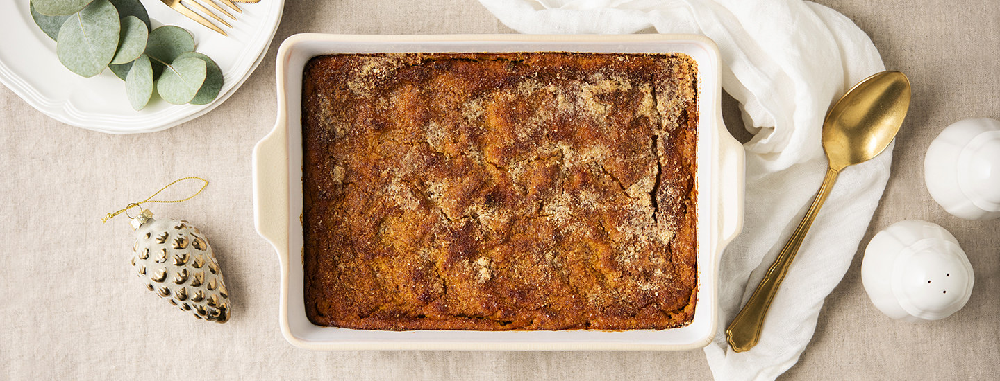 Bataatti-porkkanalaatikkoa valkoisessa uunivuoassa. Ympärillä on joulukoristeita ja kultainen lusikka. K-Ruoka jouluresepti.