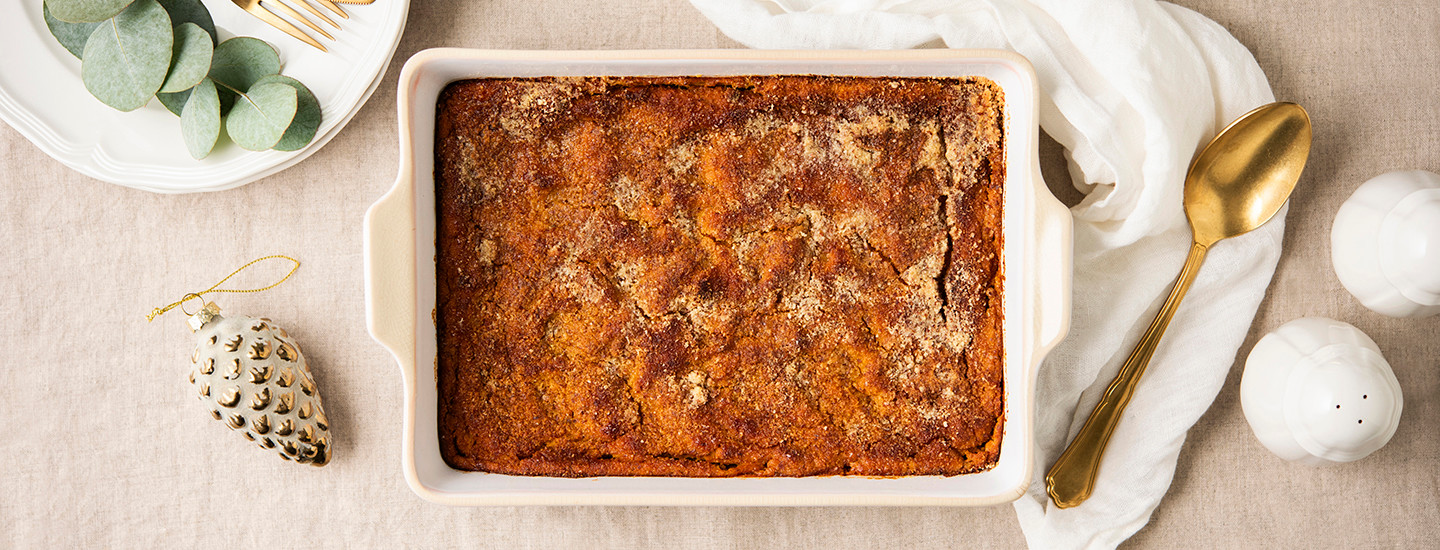 Bataatti-porkkanalaatikkoa valkoisessa uunivuoassa. Ympärillä on joulukoristeita ja kultainen lusikka. K-Ruoka jouluresepti.