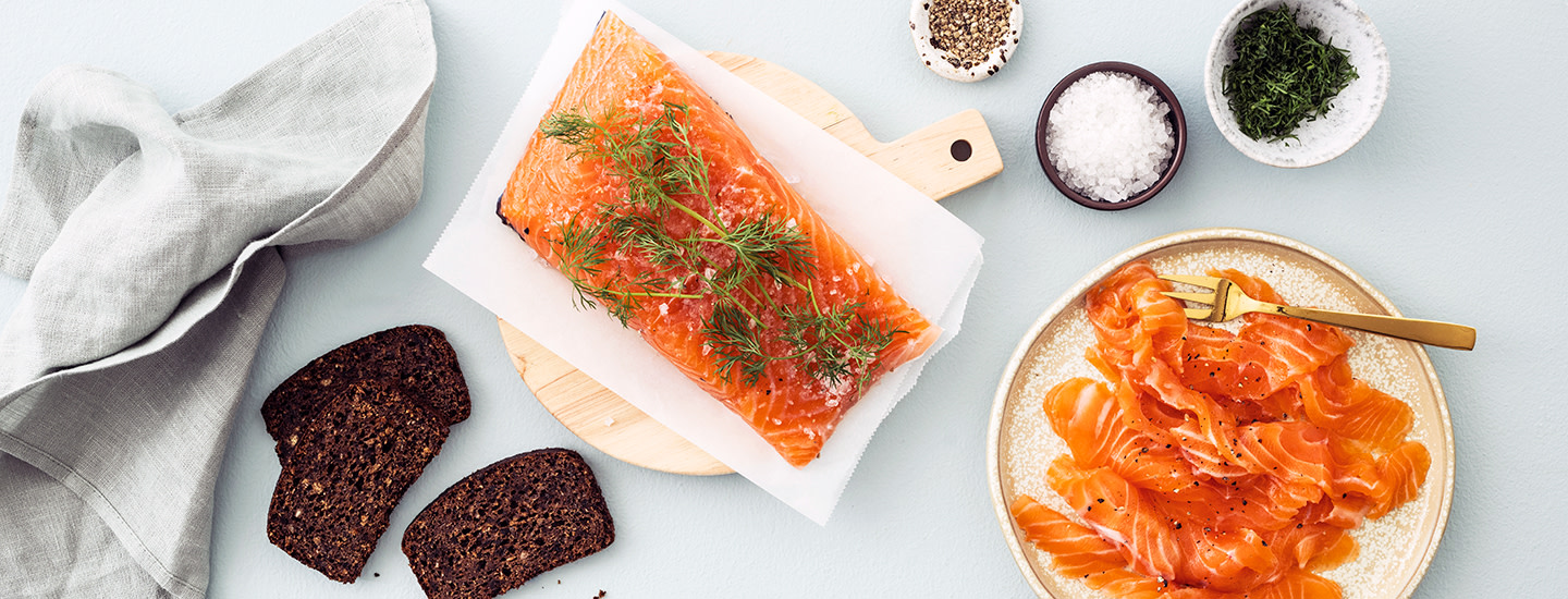 Graavattua lohta leikkuulaudan päällä. Leikkuulaudan oikealla puolella on lautanen, jossa on graavilohta siivutettuna. K-Ruoka lohiresepti.