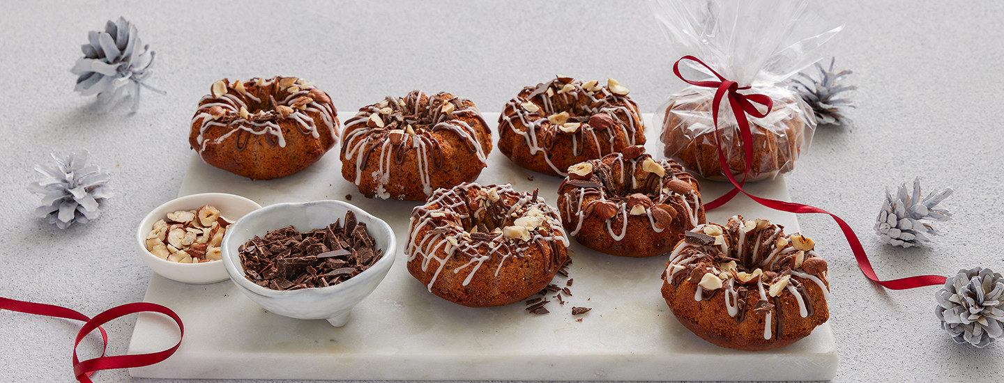 Minitaatelikakkuja valkoisella kivitarjottimella. Minitaatelikakkujen vieressä on kaksi pientä valkoista kulhoa, joissa on pähkinämurua ja suklaamurua. Yksi minitaatelikakuista on paketoitu läpinäkyvään sellofaniin. K-Ruoka leivontaresepti.