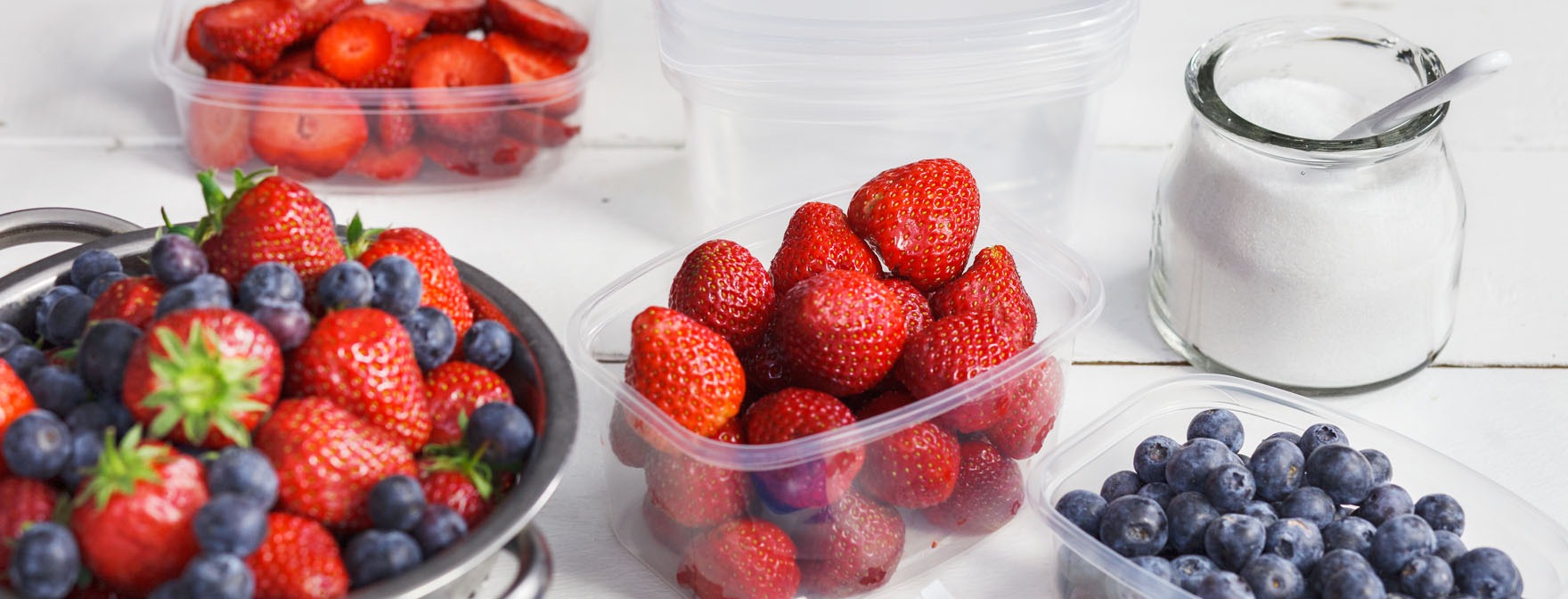 Tuoreita mansikoita ja mustikoita muovirasioissa, joita valmistellaan pakastukseen.