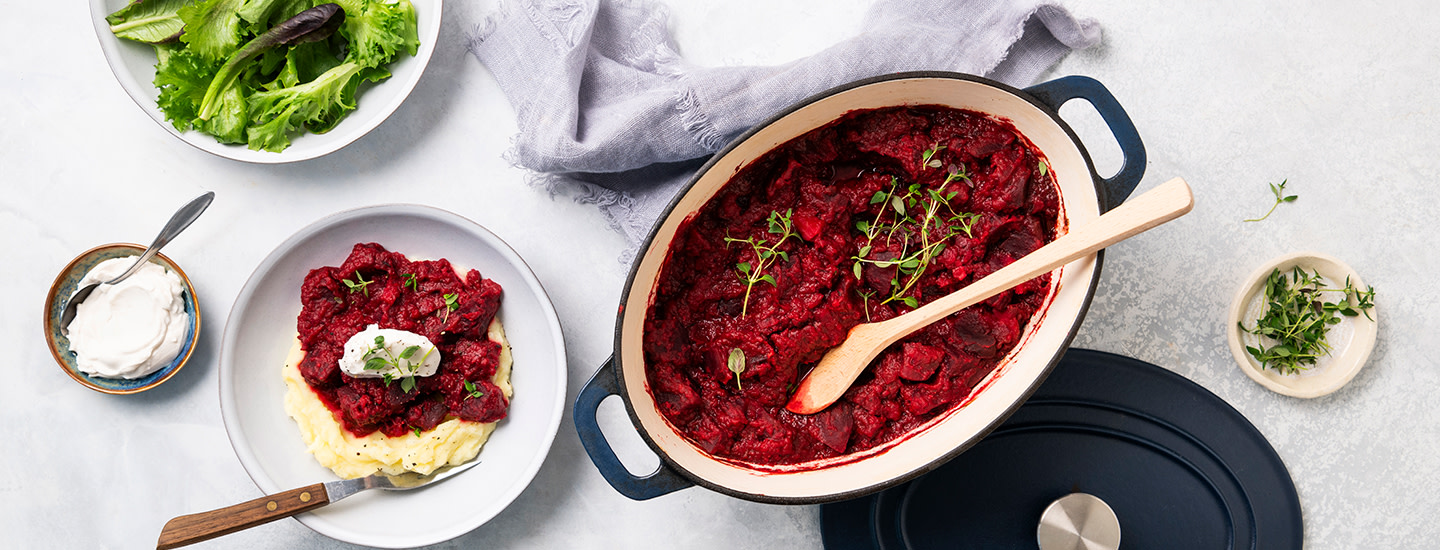 Punajuuripataa ovaalinmuotoisessa uunipadassa. Uunipadan vieressä on pyöreä lautanen, jossa on perunamuusia ja punajuuripataa. K-Ruoka punajuuriresepti.