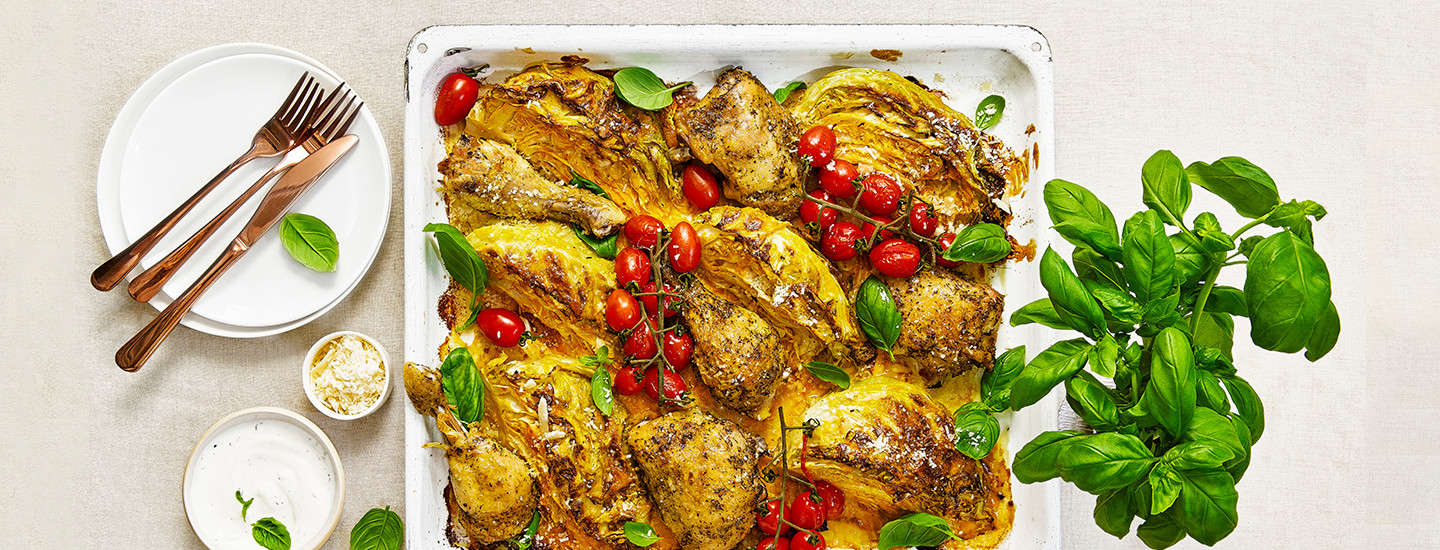 Kaalilohkoja ja kanapaloja valkoisella pellillä. Kaalien ja kanapalojen välissä on miniluumutomaattiterttuja ja tuoretta basilikaa. Kaalilohkot ja kanat on marinoitu keltaisella cheddar-sinappikastikkeella. K-Ruoka arkiruokaresepti.