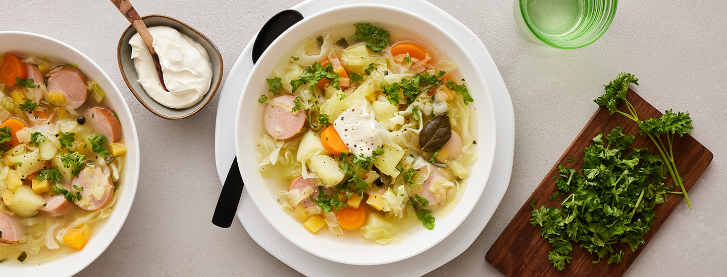 Kaali-makkarakeittoa valkoisella keittolautasella. Keiton päälle on ripoteltu tuoretta persiljaa. K-Ruoka arkiruokaresepti.