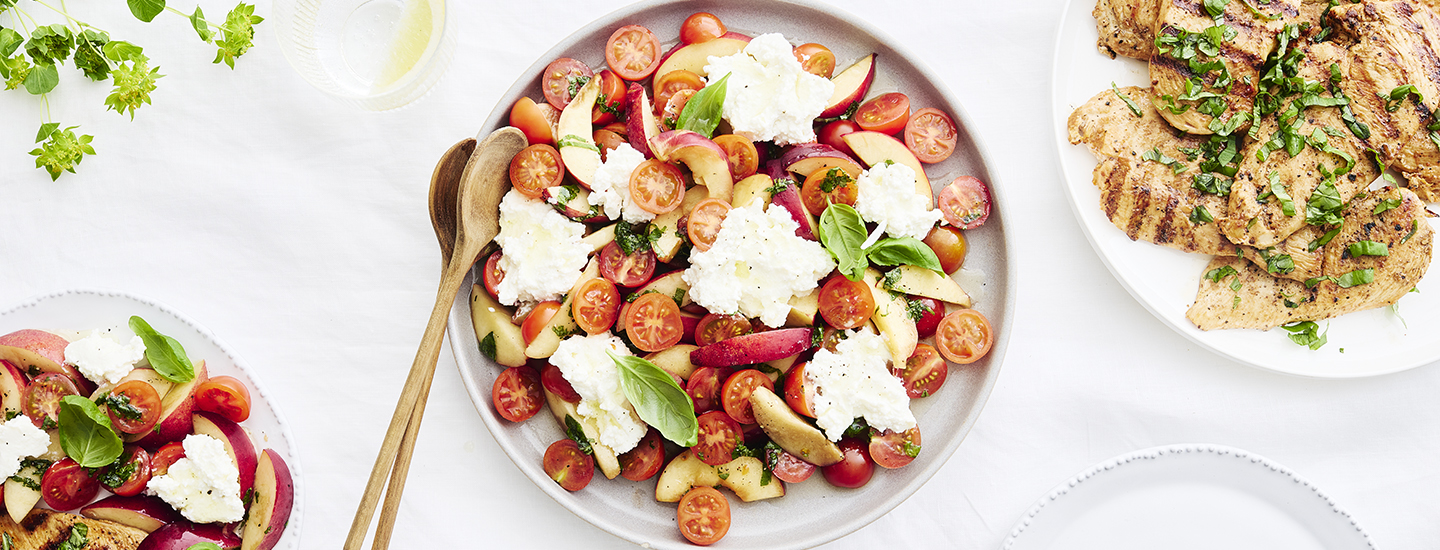 Nektariini-tomaatti-ricottasalaattia salaattilautasella. Ricottajuusto on revitty salaattiin paloiksi, kirsikkatomaatit on puolitettu. Nektariinia on salaatissa lohkoina. Salaatin päälle on ripoteltu mustapippuria ja tuoreita basilikan lehtiä. K-Ruoka salaattiresepti.