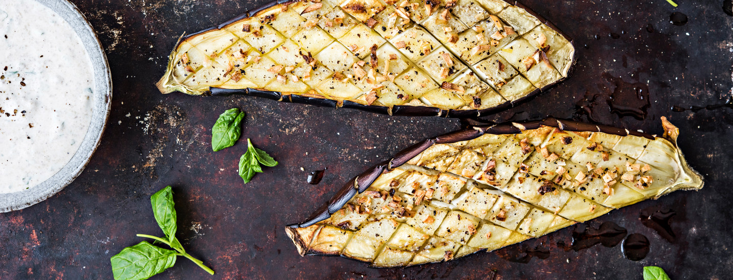 Paahdettuja munakoisoja tummalla tarjoilualustalla. Munakoisoihin on leikattu salmiakkimuotoisia viiltoja ja niiden päälle on ripoteltu mausteita. K-Ruoka grilliresepti.