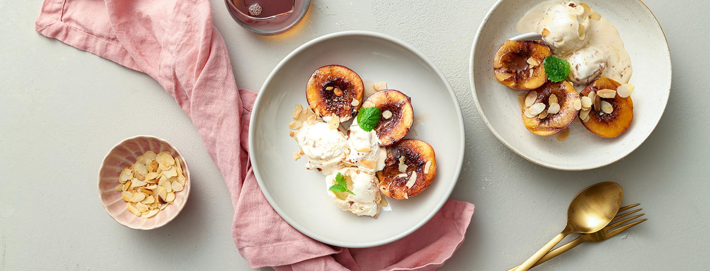 Grillattuja nektariineja vaaleanharmaalla lautasella vaniljajäätelön kanssa.