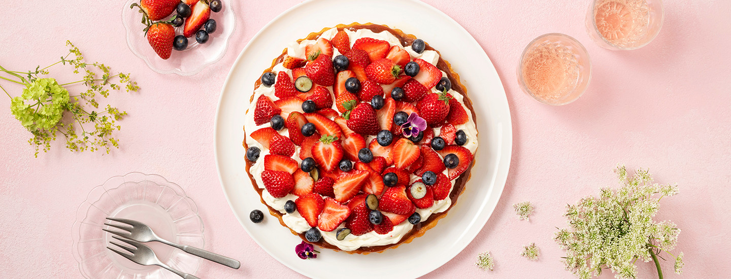 Tuoreita marjoja ja mascarpone-vaniljavaahtoa makean piirakkapohjan päällä. Mascarpone-vaniljavaahtokerroksen alla on kerros mansikka-raparperihilloa. Kakku on koristeltu syötävillä orvokeilla. K-Ruoka jälkiruokaresepti.