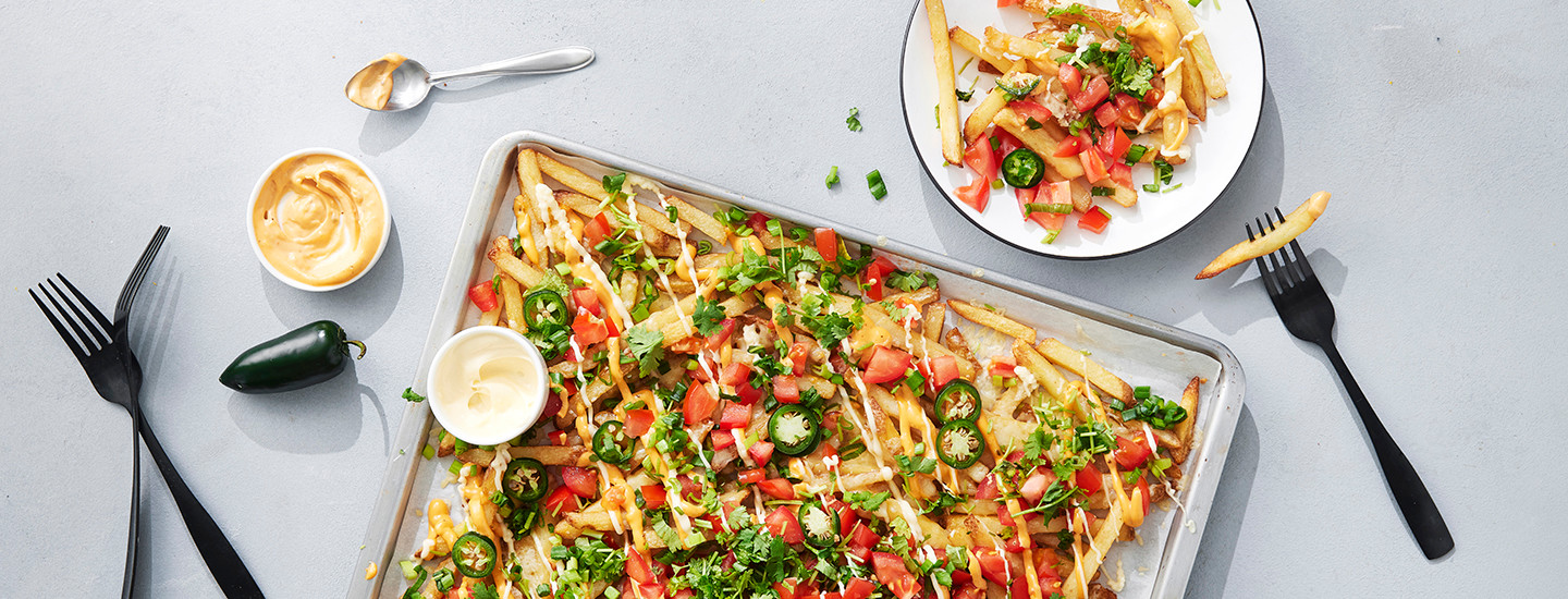 Loaded fries eli överiranskalaiset uunipellillä. Pellillä on ranskalaisia, tomaattikuutioita, jalapenosiivuja, kevätsipulia ja tuoretta korianteria. Ruoan päälle on lisätty erilaisia kastikkeita. K-Ruoka resepti.