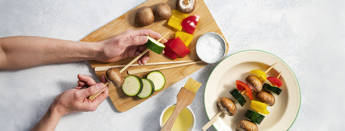 Ruskeita herkkusieniä, paprikalohkoja ja kesäkurpitsaviipaleita puisissa vartaissa.