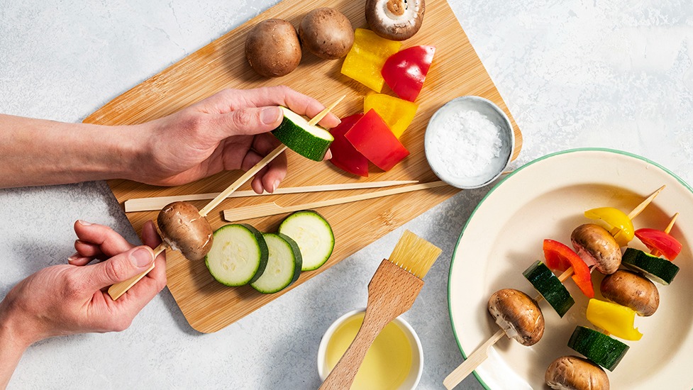 Ruskeita herkkusieniä, paprikalohkoja ja kesäkurpitsaviipaleita puisissa vartaissa.