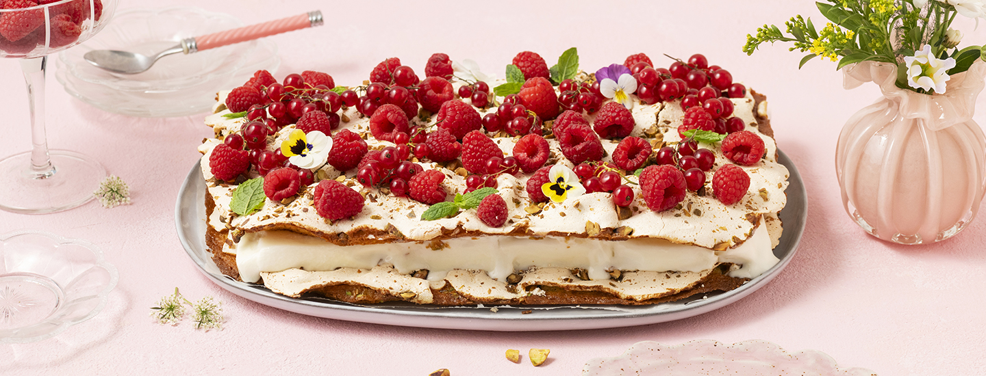 Jäätelöbritakakku tarjoilulautasella. Britakakkupohjien välissä on vaniljajäätelöä. Kakku on koristeltu tuoreilla marjoilla ja syötävillä orvokeilla. K-Ruoka jälkiruokaresepti.