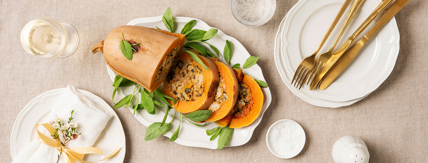 Kurpitsapaisti valkoisella tarjoilulautasella. Kurpitsa on kaiverrettu sisältä ja sen sisään on lisätty linssitäytettä. Kurpitsapaistia on leikattu kolmeksi siivuksi lautaselle. Kurpitsan ympärille on aseteltu salvianlehtiä. K-Ruoka vegaaninen jouluresepti.