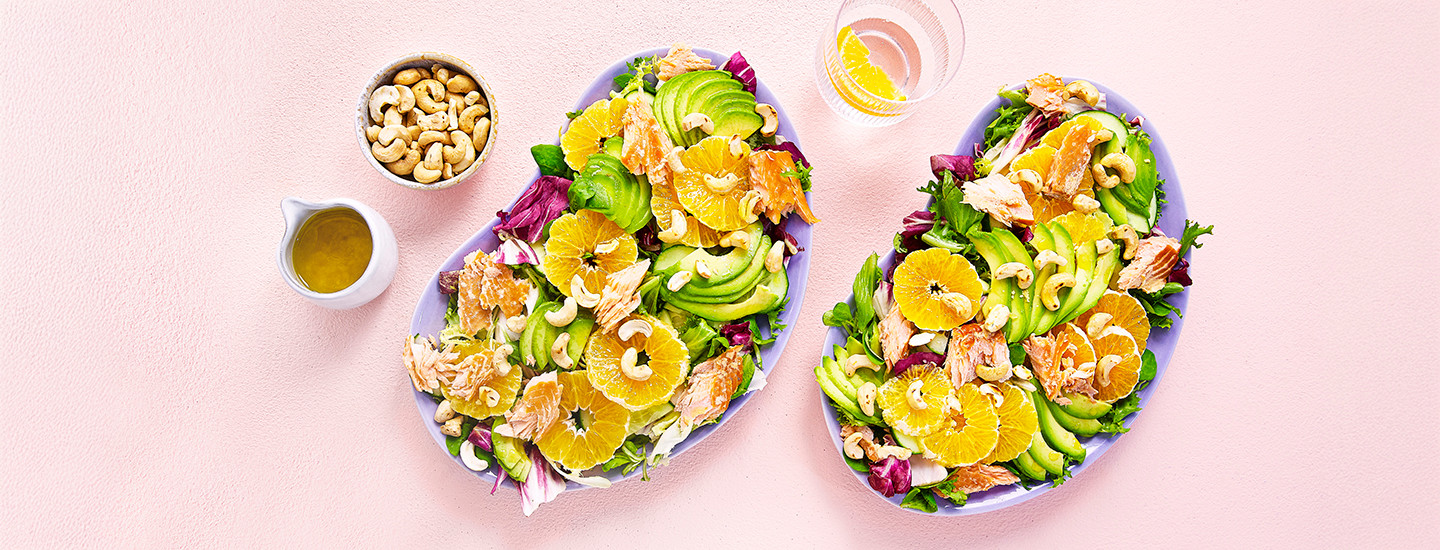 Avokado-lohisalaattia kahdella violetilla lautasella. Salaatissa on salaatinlehtien päällä lämminsavustettua lohta, klementiinisiivuja, avokadoa ja cashewpähkinöitä. K-Ruoka salaattiresepti.