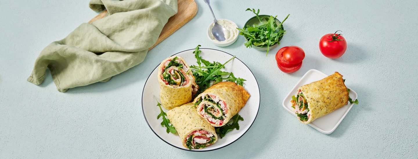 Raejuusto-flatbreadin puolikkaita valkoisessa kulhossa. Yksi flatbreadin puolikas on kulhon oikealla puolella. Kulhon yläpuolella on kuppi tuoretta rucolaa ja kaksi kokonaista tomaattia. K-Ruoka arkiresepti.