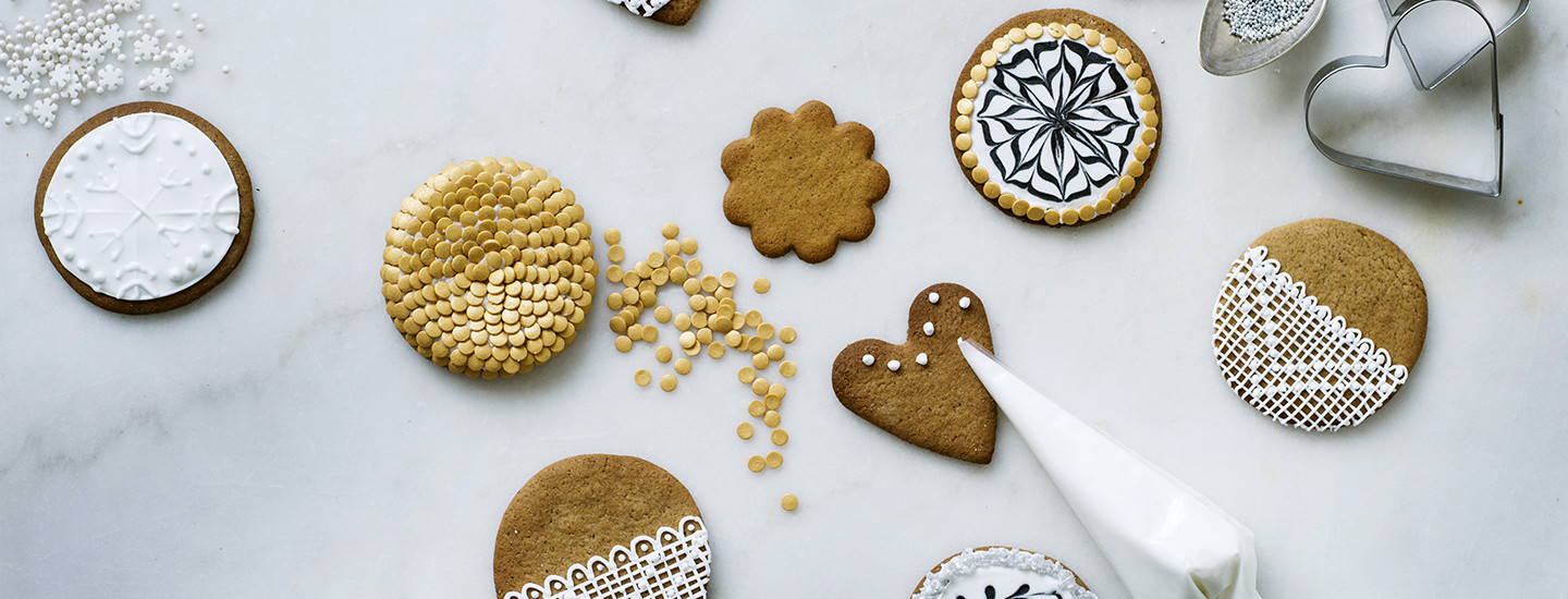 Pipareita valkoisella pöydällä. Pipareissa on erilaisia kuorrutuksia, jotka on tehty valkoisella sokeripikeerillä. K-Ruoka jouluresepti.