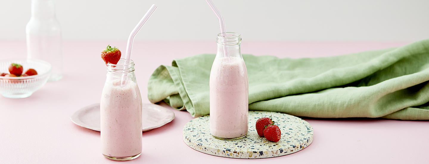 Raejuustosmoothieta kahdessa eri lasipullossa. Pulloihin on laitettu pillit. Toisen pullon suunreunassa on tuore mansikka. K-Ruoka smoothieresepti.