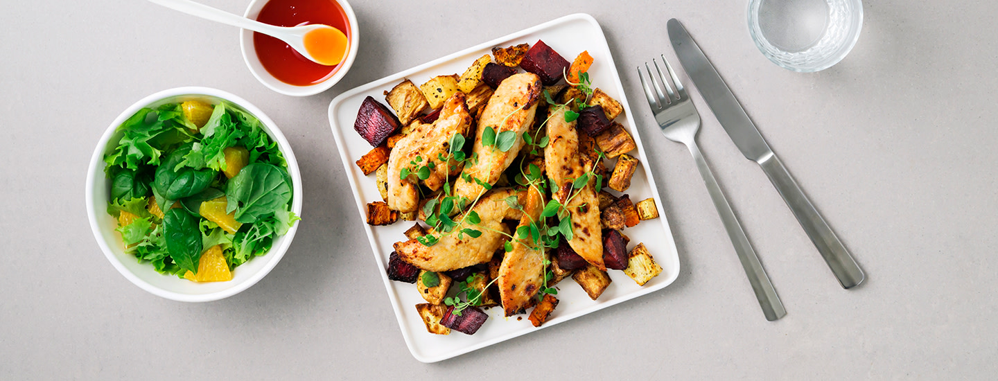 Hot honey -maustettuja kanan ohutleikkeitä lautasella. Kanaleikkeiden alla on paadettuja juureksia kuutioituna. Annoksen päälle on lisätty tuoreita yrttejä. K-Ruoka arkiruokaresepti.