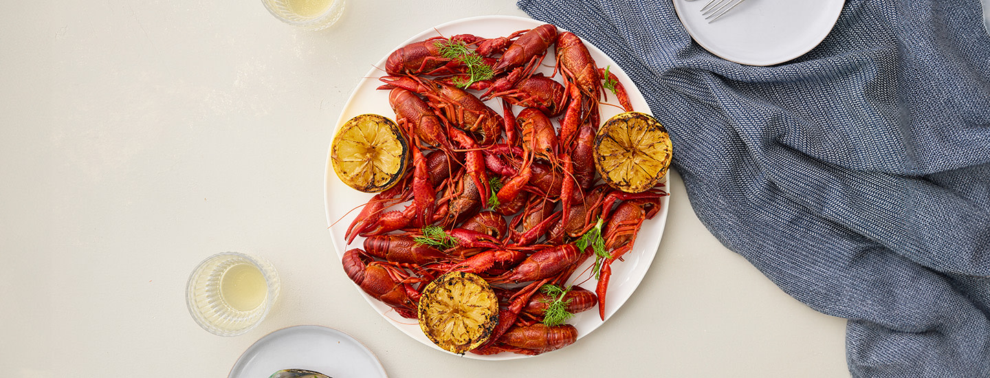 Keitettyjä rapoja pyöreällä lautasella vaalealla alustalla. K-Ruoan kuvituskuva.