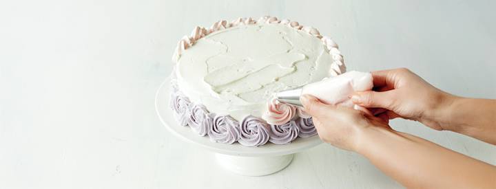 Täytekakku, jonka päälle on levitetty kermavaahtoa. Kakun sivuun on tehty vaaleanliiloja ja vaaleanpunaisia ruusupursotuksia.