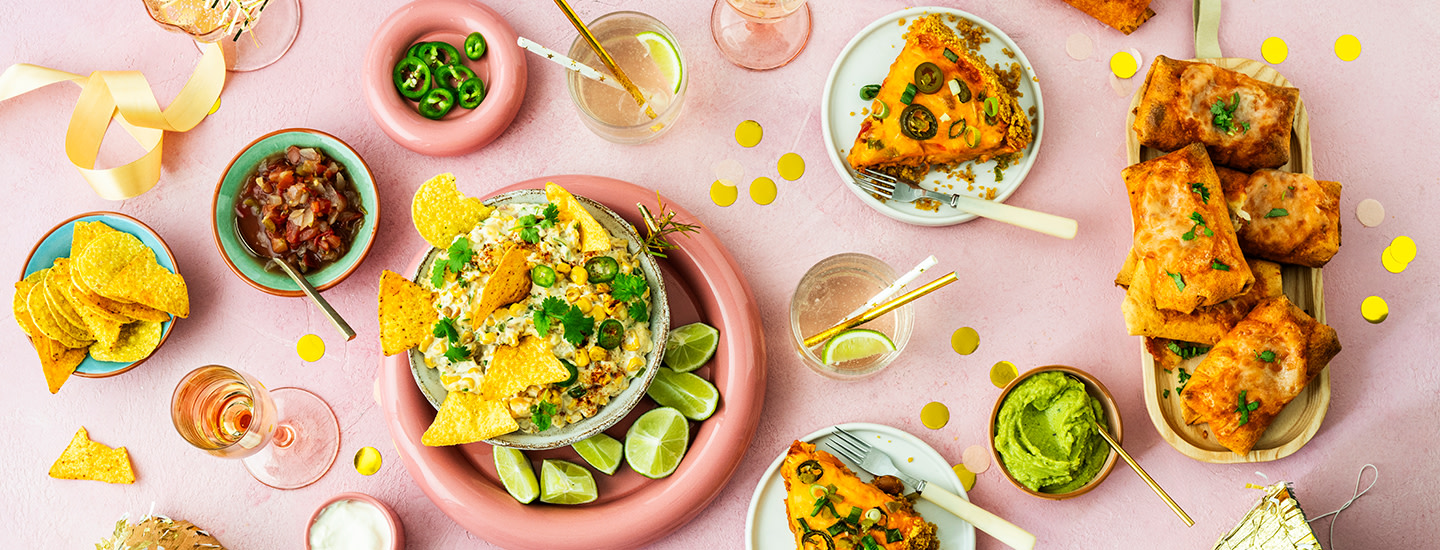 Erilaisia texmex-ruokia pöydälle aseteltuna. Pöydällä on maissidippiä nachosipsien kanssa, kaksi palaa nachopiirakkaa, burritoja ja erilaisia kastikkeita. K-Ruoka texmex.